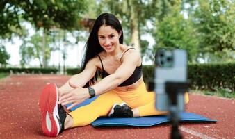 Fit smiling active woman using a smartphone for training, vlog or courses online in the park. Tutorial online concept photo