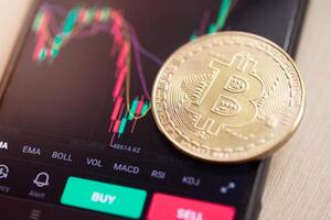 Bitcoin coin on the background of a smartphone screen with a graph of fall of cryptocurrency market on the exchange. Bear market, dump, losses concept. photo