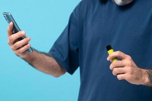 Green disposable electronic cigarette and phone in a man's hand. Modern online communication. on blue background photo