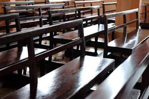 Vintage long wooden chairs for sitting and praying for blessings in Christian churches. Rows of church benches in sunlight photo