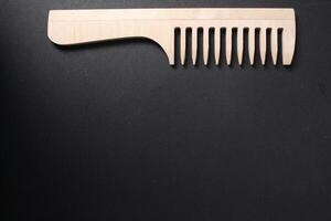 Concept of selection of tools for hair care. Wooden natural comb on black background. Hair Materials, Combs, Hairdresser's Tools photo