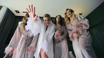 Gorgeous Bride and three Bridesmaids Waving Hands on Camera. Joyful Friends in Silk Bathrobes Dancing together on Hotel Bed. Women Having Fun during Morning Preparation for Wedding video