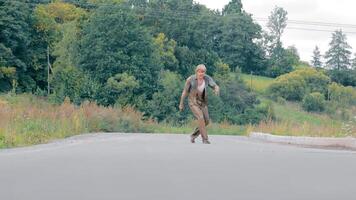 Drunk Beggar dressed in Old Dirty Clothes Walking and Staggering on Asphalt Road. Male Homeless Covered with Swamp Alone at Countryside. Depressed Man Drinking Alcohol while Suffering from Poor Life video