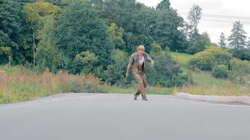 ubriaco mendicante vestito nel vecchio sporco Abiti a piedi e sbalorditivo su asfalto strada. maschio senza casa coperto con palude solo a campagna. depresso uomo potabile alcool mentre sofferenza a partire dal povero vita video