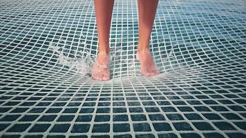 Close-up of the baby girl's legs swimming in the water while standing on a knitted net in slow motion. video