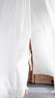 hermosa mujer con largo pelo en blanco ropa camina y poses entre blanco y aireado cortinas en un desván habitación video