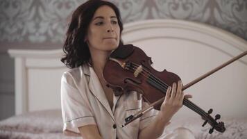 beautiful girl playing the violin while sitting on the bed at home, hand-held shooting, close-up video