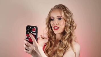 A young woman in a red dress takes a selfie with long blond hair and makeup. The girl is smiling and looking at the camera close-up video