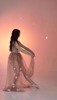 A young woman, a ballerina girl dancing, gently moving her arms and fingers on a pink background in a studio, slowmo, medium. Lady brown-haired woman with long hair video