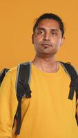 Portrait of confident indian man holding thermal backpack, crossing arms, studio background. Radiant nonchalant delivery person prepared to deliver takeaway food to customers, camera A video