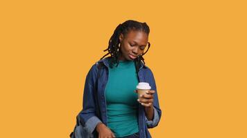 Tired girl travelling with suitcase, drinking coffee to wake up. Sleepy woman using caffeinated beverage to gain energy, going abroad with briefcase, studio background, camera A video