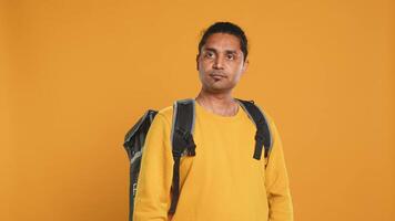 Portrait of upbeat indian man holding thermal backpack, isolated over studio background. Friendly cheerful person prepared to deliver takeaway food to customers, camera A video