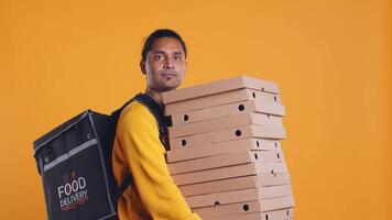 Indian delivery worker offering takeaway order to customer paying with debit card. Client buying meal from courier, swiping card on POS device, studio background, camera B video