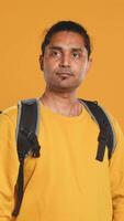 Portrait of man holding thermal backpack, crossing arms, ready to fulfill orders, studio backdrop. Calm food delivery service worker prepared to do delivery to customers, camera A video