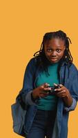 vertical eufórico africano americano mujer jugando intenso juego de azar consola juego, celebrando ganar, estudio antecedentes. extático joven niña utilizando controlador, emocionado después siendo victorioso en videojuego, cámara si video