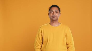 Portrait of cheerful friendly indian man smiling, looking pleased, isolated over yellow studio background. Happy expressive asian person grinning, feeling satisfied, camera A video