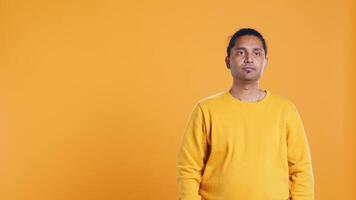 Portrait of cheerful friendly indian man smiling, looking pleased, isolated over yellow studio background. Happy expressive asian person grinning, feeling satisfied, camera B video