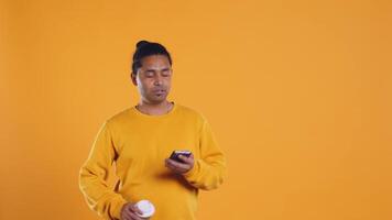 Indian man enjoying fresh coffee from disposable paper cup early in the morning to wake up and be energized. Person drinking hot beverage from recycled takeaway cup, studio background, camera B video