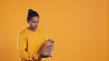 Indian pizza delivery worker getting takeaway order out of thermal backpack, giving it to client paying with card. Courier offering lunch paper bag and POS to customer, studio background, camera B video