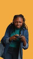 verticale africano americano gamer Tenere controllore, focalizzata su finitura difficile video gioco livello. donna gioco con gamepad, soluzione missioni, isolato al di sopra di studio sfondo, telecamera B