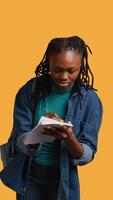 Vertical Girl with bad eyesight squinting eyes, trying to read lecture information and take notes at school on notepad, studio background. Student struggling to understand university class material, camera B video