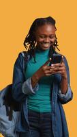 Vertical Portrait of overjoyed teenager reading messages on phone, delighted after receiving good news. Woman excited by SMS on smartphone, celebrating, studio background, camera B video