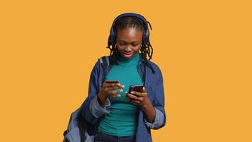 African american teenager adding payment method on website, isolated over studio background. Young girl wearing headphones, doing internet shopping, typing credit card information on phone, camera A video