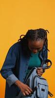 Vertical Portrait of smiling woman rummaging through backpack, looking for school notebook and notes, isolated over studio background. Cheerful girl taking out university supplies out of rucksack, camera B video