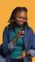 Vertical African american motivational speaker talking in microphone, addressing audience, holding speech, studio background. Inspiring woman using mic to present life lectures, camera A video