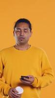 Indian man enjoying fresh coffee from disposable paper cup early in the morning to wake up and be energized. Person drinking hot beverage from recycled takeaway cup, studio background, camera B video