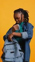 Vertical Portrait of happy woman searching through backpack, looking for school materials, studio background. Jolly girl taking out university supplies out of rucksack, preparing for college, camera B video