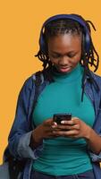 Vertical Smiling woman discussing with friends during teleconference meeting using smartphone and headphones, studio background. Girl catching up with mates during online videocall on mobile phone video