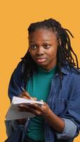 Vertical Girl with bad eyesight squinting eyes, trying to read lecture information and take notes at school on notepad, studio background. Student struggling to understand university class material, camera A video