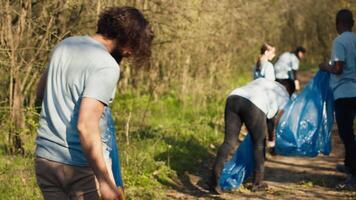 team av volontärer rengöring de skog område från sopor och plast, samlar skräp med tång och påsar. aktivister håller på med frivillig arbete till bevara naturlig livsmiljö, olaglig dumpning. kamera a. video