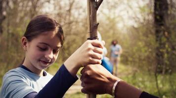 Kind und ihr Freund sind Pflanzen ein klein Baum im das Wald, beitragen zu Tierwelt und Natur Erhaltung. jung Mädchen tun freiwillig Arbeit mit Teenager, Umwelt Bildung. Kamera b. video