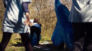 africano americano niña cosecha arriba basura con un largo garra y basura bolsas, limpieza bosque habitat y luchando ilegal dumping con un equipo de voluntarios activista coleccionar basura. cámara b. video