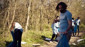 hombre activista utilizando tenazas a agarrar basura y el plastico desperdiciar, cosecha arriba basura y limpieza el bosque área. voluntario clasificación basura y reciclaje él, conservación el naturaleza. cámara b. video