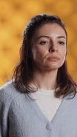 Vertical Portrait of relaxed woman posing, looking at camera, isolated over yellow studio background. Caucasian person dressed in casual attire standing, feeling confident, camera A video