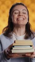 Vertical Cheerful woman happy to receive stack of books from friend, excited to read them, studio background. Joyous bookworm delighted by gift of novels pile from mate, eager to enjoy them video