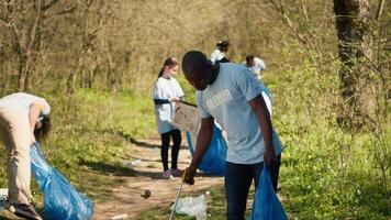 africano americano uomo volontario raccolta spazzatura e plastica rifiuto con pinza, afferrando sciocchezze e raccolta differenziata nel un' spazzatura disposizione. attivista la lotta contro foresta inquinamento e illegale dumping. telecamera un. video