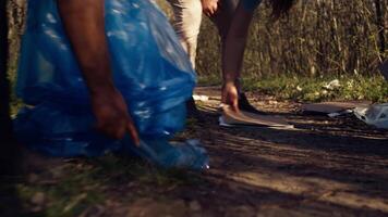 People picking up trash and plastic bottles from the forest area, protecting the natural environment and doing voluntary work. Activists group cleaning the woods, recycling waste. Camera B. video