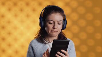 Woman wearing headphones, practicing new language using internet app on digital tablet, isolated over studio background. Person repeating foreign words, reading them on device video