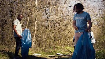 Jeune bénévole Faire litière nettoyer avec une longue griffe à saisir poubelle et boutique il dans une des ordures sac, transaction avec la pollution un illégal dumping problème. activiste protéger Naturel écosystème. caméra b. video