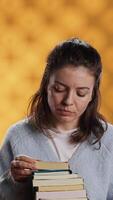 vertical retrato de mujer hojeada mediante apilar de libros de texto, reunión información para colegio examen, aislado terminado estudio antecedentes. persona buscando necesario curso para examen en pila de libros, cámara un video