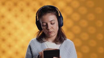 vrouw lezing ebook Aan ereader en luisteren muziek- inkoop boeken online. persoon met tablet op zoek naar kopen digitaal roman met credit kaart, horen liedjes in koptelefoon, studio achtergrond, camera een video