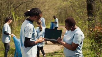 African american women use laptop with greenscreen during a litter cleanup activity to protect the environment and preserve nature. Volunteers cleaning up trash, ecological justice. Camera A. video