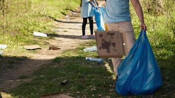 joven voluntario haciendo camada limpiar con un largo garra a agarrar basura y Tienda eso en un basura bolsa, relación comercial con contaminación un ilegal dumping problema. activista proteger natural ecosistema. cámara una. video