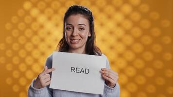 Woman holding message in hands urging people to read more, talking about importance of lecture, isolated over studio background. Bookworm promoting literacy concept, camera B video