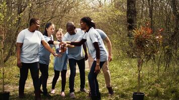 Cheerful proud team of activists join forces to clean a forest, celebrating their volunteering work by connecting hands together. Happy people showing responsibility for the environment. Camera B. video