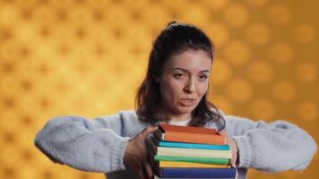 Woman choosing between physical books and ebooks, favoring ereader for lightness, studio background. Bookworm picking digital literature on tablet in front of heavy stack of novels, camera A video